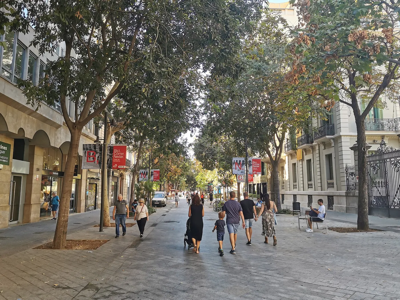 Η οδός Consell de Cent στη Βαρκελώνη μετά την ανάπλαση: μεγάλος πλακόστρωτος χώρος, δέντρα, παγκάκια, κόσμος περπατά στο πρώην οδόστρωμα